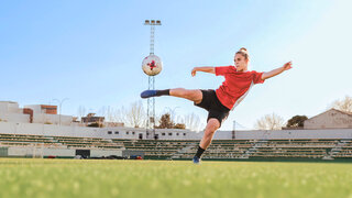 Eine Fußballerin liegt quer in der Luft und schießt einen Ball.