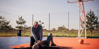 Ein Mann reanimiert einen anderen Mann auf einem Basketballplatz mit einer Herzdruckmassage.