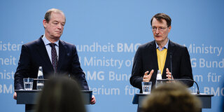 Michael Hallek, links im Bild, und Karl Lauterbach sprechen auf einem Podium.