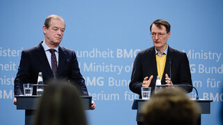Michael Hallek, links im Bild, und Karl Lauterbach sprechen auf einem Podium.