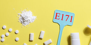 Eine Illustration zeigt Lebensmittel und Medikamente mit weißer Färbung durch Titandioxid, außerdem ein Schild mit der Aufschrift E171.