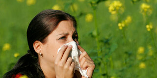 Eine Frau steht vor einer blühenden Wiese und putzt sich die Nase.