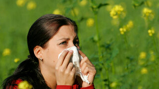 Eine Frau steht vor einer blühenden Wiese und putzt sich die Nase.