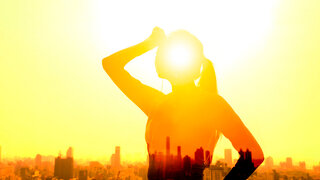 Eine Frau hält sich erschöpft die Hand an die Stirn, während die Sonne über ihr strahlt.