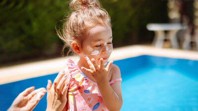 Ein Kind verteilt Sonnencreme im Gesicht.