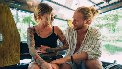 Junges Paar im Camping-Bus, sie hält sich den Bauch, er streichelt sie beruhigend.
