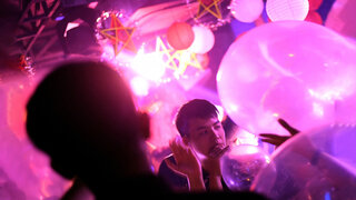 Jugendliche halten sich auf einer Party einen Luftballon an den Mund.