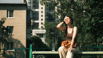 Eine Frau sitzt im Sonnenschein auf einer Bank und wischt sich den Schweiß mit einem Tuch von der Stirn.