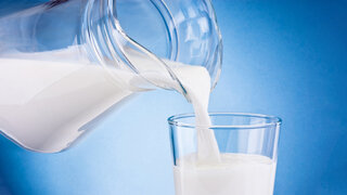 Aus einem Krug wird Milch in ein Glas eingeschenkt.
