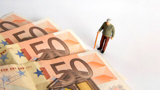 Ein Miniaturmodell eines älteren Mannes vor Geldscheinen.