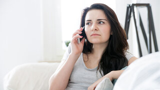 Eine Frau hält ein Telefon ans Ohr und hört skeptisch zu.