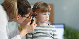 Ärztin untersucht das Ohr eines kleinen Mädchens mit dem Otoskop