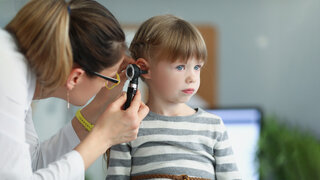 Ärztin untersucht das Ohr eines kleinen Mädchens mit dem Otoskop