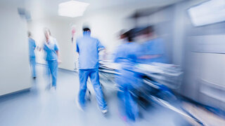 Verschwommenes Bild von einem Krankenhausflur in dem Personal in blauen Kitteln ein Krankenbett schieben