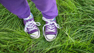 Ein Kind steht in Schuhen und mit langer Hose im Gras.