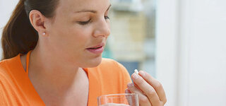 Frau nimmt Tablette mit einem Glas Wasser ein 