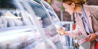 Frau vor Gefriertruhe im Supermarkt: Sie hält abgepacktes Fleisch und Geflügel in der Hand