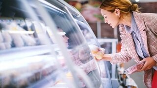 Frau vor Gefriertruhe im Supermarkt: Sie hält abgepacktes Fleisch und Geflügel in der Hand
