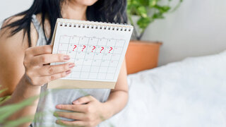 Junge Frau sieht auf einen Kalender und greift sich an den Bauch.