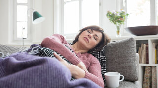 Langzeitfolgen von Infektionskrankheiten Frau Erschöpft Müde Krank Sofa ausruhen Tee Trinken 50 Jahre Decke 